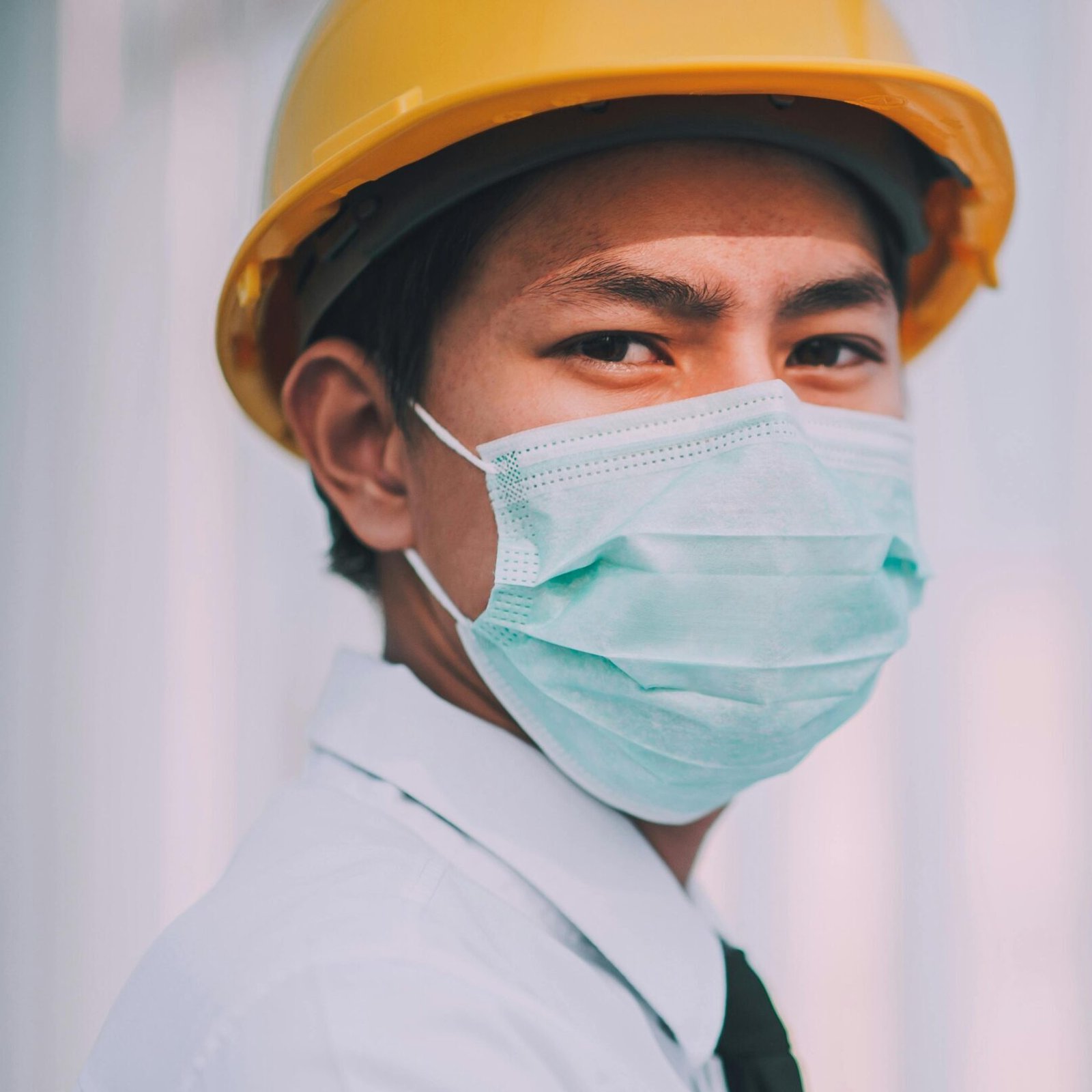Young engineer in a hard hat and mask examines blueprints for construction.